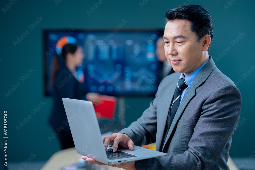 Handsome business man and suit holding the laptop in his hands and writing something. Side view, standing confident in the office in front of his team. Handsome business man and suit holding the laptop in his hands and writing something. Side view, standing confident in the office in front of his team.