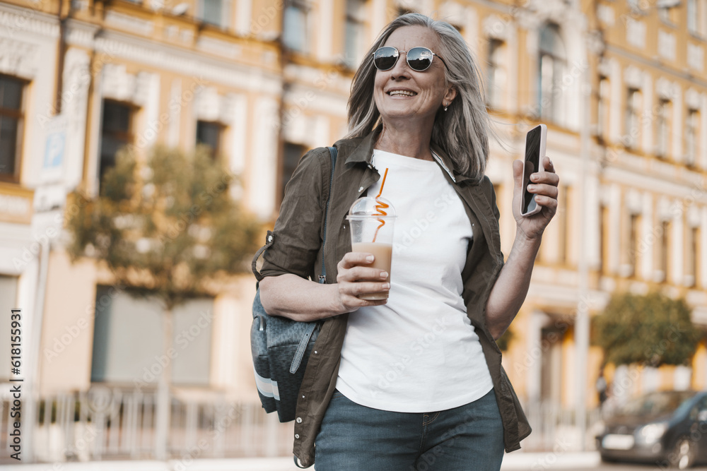 Obraz premium concept of travel in old age, featuring mature woman enjoying trip in old city of Europe. senior woman seen appreciating view of city and capturing moment by taking photos on mobile phone.