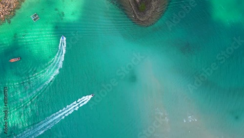 Top view of boats gliding along the beautiful turquoise water near the coastline of a tropical island in Thailand. 