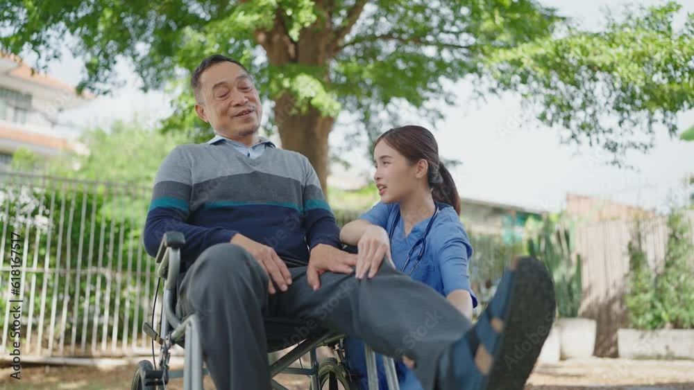 Asian woman nurse takes care of adult male patient sitting on wheelchair at outdoors. Caring and support for leg injuries of male patient. Retirement, physiotherapy and healthcare Asian woman nurse takes care of adult male patient sitting on wheelchair at outdoors. Caring and support for leg injuries of male patient. Retirement, physiotherapy and healthcare