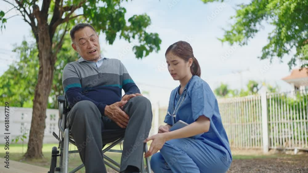 Asian woman nurse using tablet for checking leg injuries of male patient while sitting on wheelchair at outdoors. Retirement, physiotherapy and health care Asian woman nurse using tablet for checking leg injuries of male patient while sitting on wheelchair at outdoors. Retirement, physiotherapy and health care