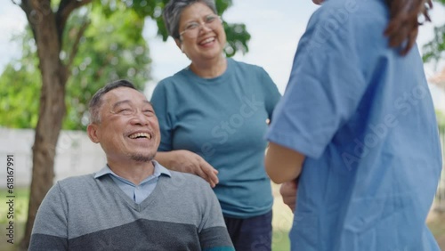 Happy asian adult male patient enjoy talking with his wife and woman caregiver nurse while sitting on wheelchair relaxing at hospital park. Retirement, physiotherapy and health care