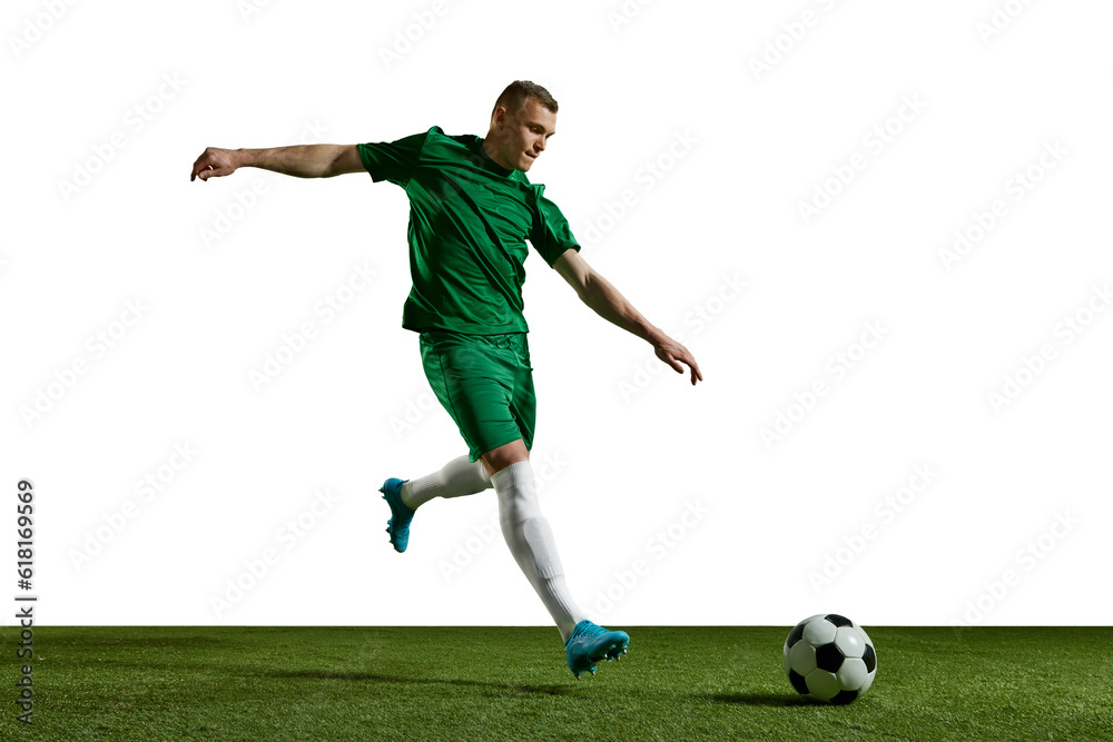 Young man in green uniform, football in motion, playing, kicking ball on sports field against white background. Concept of professional sport, action, lifestyle, competition, hobby, training, ad