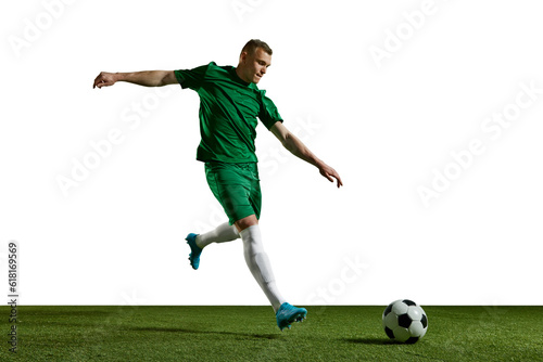 Young man in green uniform, football in motion, playing, kicking ball on sports field against white background. Concept of professional sport, action, lifestyle, competition, hobby, training, ad © master1305