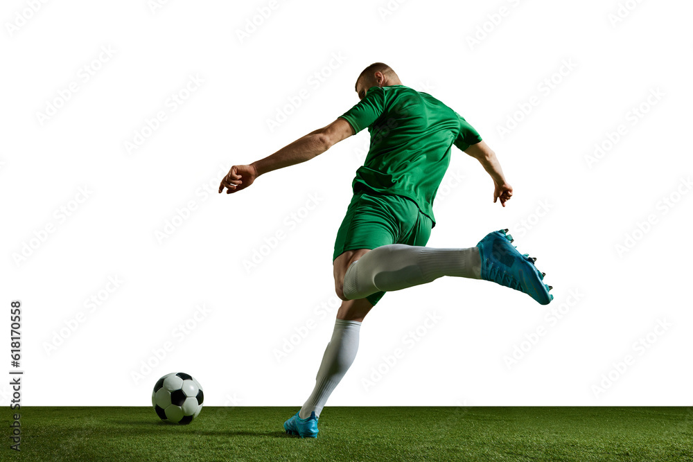 Young man, football player in green uniform in motion, kicking ball, training, playing against white background. Concept of professional sport, action, lifestyle, competition, hobby, training, ad