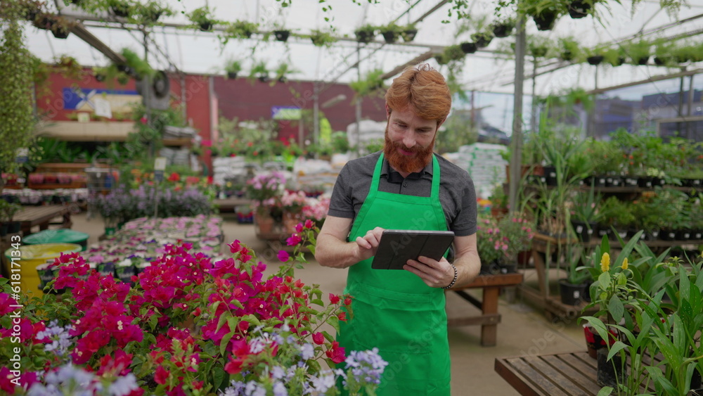 Young employee using tablet standing inside Local Business. A male redhair caucasian employee holding modern device browsing inventory at Flower Shop Young employee using tablet standing inside Local Business. A male redhair caucasian employee holding modern device browsing inventory at Flower Shop
