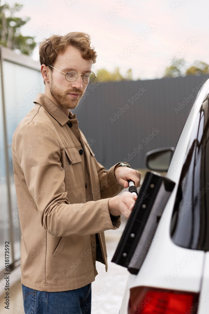 Portrait of smiling man using window scraper, wiping car. Vehicle washing, regular cleaning concept Portrait of smiling man using window scraper, wiping car. Vehicle washing, regular cleaning concept