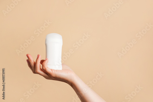 Female hand holds white body deodorant on beige background, copy space