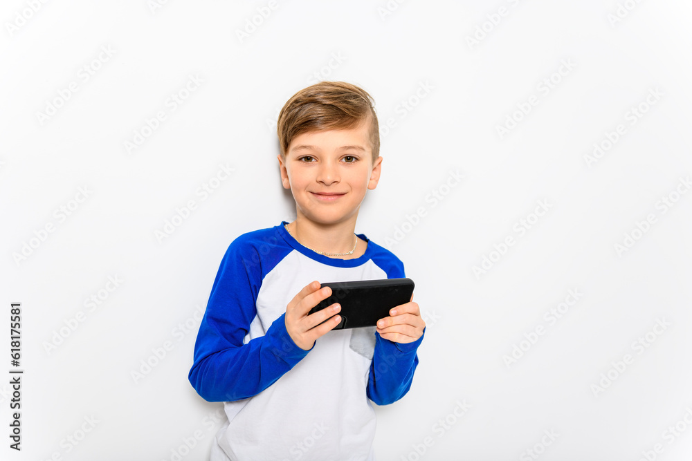Cute little boy playing game over smartphone on white studio background. Cute little boy playing game over smartphone on white studio background.