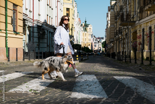 Young woman walking with dog in the town, lifestyle with pets. Girl and australian collie on the walk dowtown, crossing the road