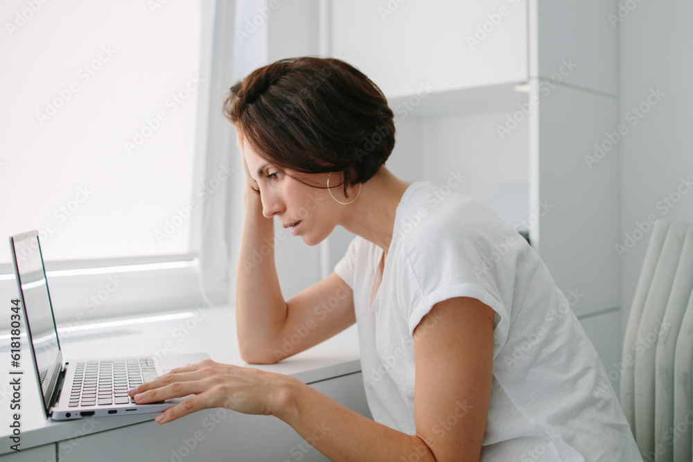 Tired, frustrated, exhausted, stressed woman sitting at desk working on laptop. Headache. Daylight work. Girl in White tshirt Tired, frustrated, exhausted, stressed woman sitting at desk working on laptop. Headache. Daylight work. Girl in White tshirt