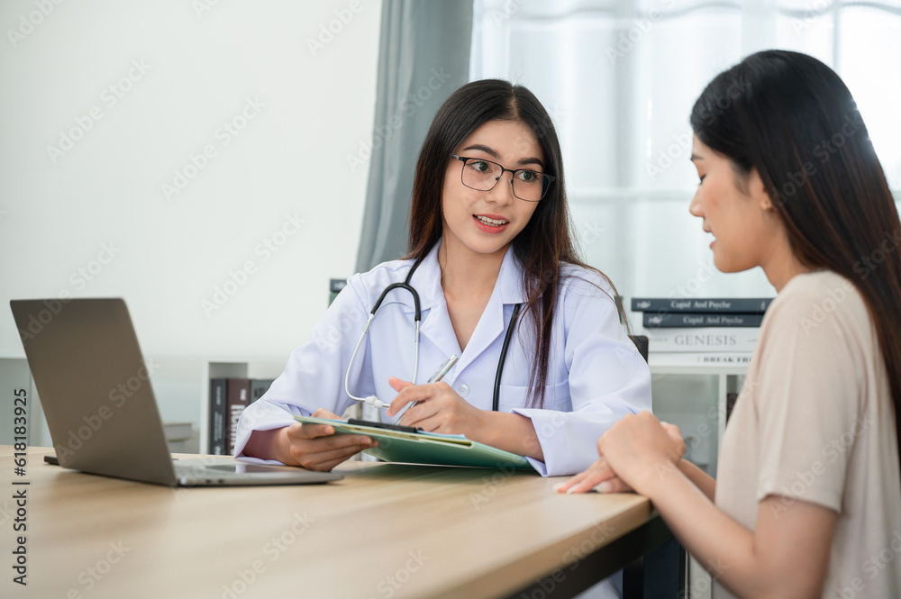 Asian female doctor working Using her laptop to consult a female patient at a medical clinic office writing a prescription on a table in a hospital Asian female doctor working Using her laptop to consult a female patient at a medical clinic office writing a prescription on a table in a hospital