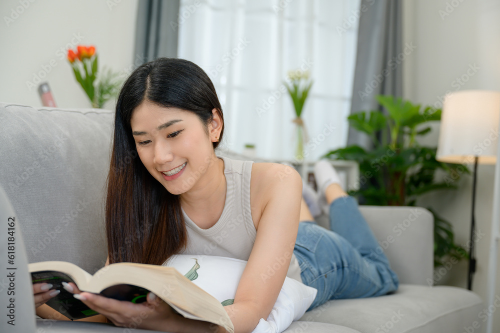 Young Asian woman reading a book at her home lying on the fabric sofa In the living room having a good time at home Young Asian woman reading a book at her home lying on the fabric sofa In the living room having a good time at home