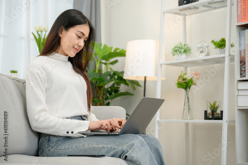 asian girl Happy freelancer sitting and typing On laptop computer keyboard on sofa in living room at home and working online with laptop computer