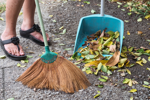 Woman use a broom sweeping leaves to dustpan on backyard