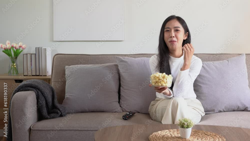 Young happy cheerful asian female eating popcorn glass bowl snack watching movie on sofa. Young happy cheerful asian female eating popcorn glass bowl snack watching movie on sofa.
