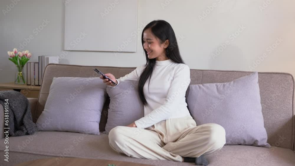 young asian woman relax on comfortable couch at home using smartphone feeling happy positive while sitting on the sofa in living room. young asian woman relax on comfortable couch at home using smartphone feeling happy positive while sitting on the sofa in living room.