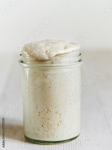 Wheat sourdough starter. Glass jar with sourdough starter on white wooden tabletop. Copy space for text or design. Vertical.