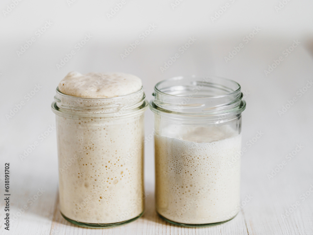 Two glass jars with wheat sourdough starters in different hydration levels. Starter 100 percent hydration - left and starter with higher hydration - right. Copy space Two glass jars with wheat sourdough starters in different hydration levels. Starter 100 percent hydration - left and starter with higher hydration - right. Copy space