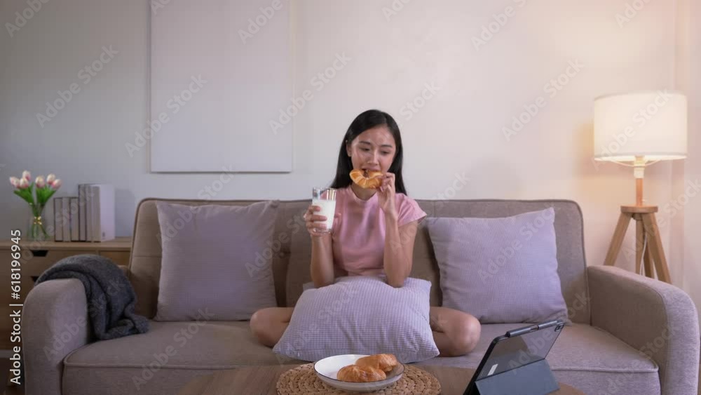 Asian woman eating breakfast meal on the table during watching movie on tablet at home in the morning, Lifestyle concept. Asian woman eating breakfast meal on the table during watching movie on tablet at home in the morning, Lifestyle concept.