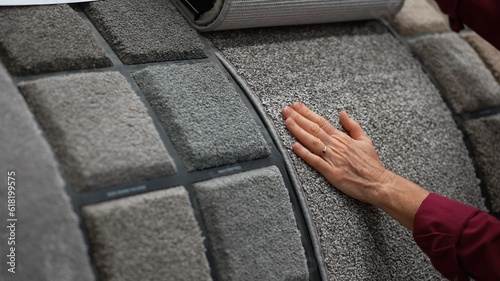 Fotografie Mature woman runs hand over carpet samples shopping in large hardware store for home renovation project