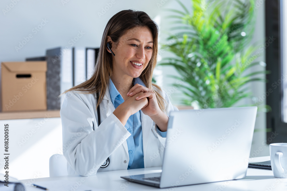 Female doctor talking with colleagues through a video call with a laptop in the consultation. Female doctor talking with colleagues through a video call with a laptop in the consultation.