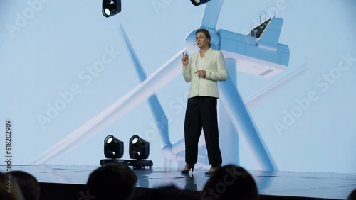 Caucasian woman female speaker presenting on the stage during ecological renewable energy conference. Future technology meetup. Talks about green energy sources, wind turbines, solar power photo