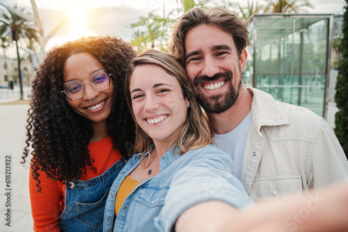 Three young adult friends smiling taking a selfie portrait and having fun together. Group of multiracial cheerful people celebrating their friendship. Two women and one man with positive expression