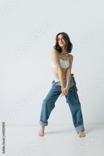 Full-length portrait of beautiful, curly, young woman with slim body posing in jeans and top against grey studio background. Concept of beauty, body and skin care, health, fitness, wellness, ad