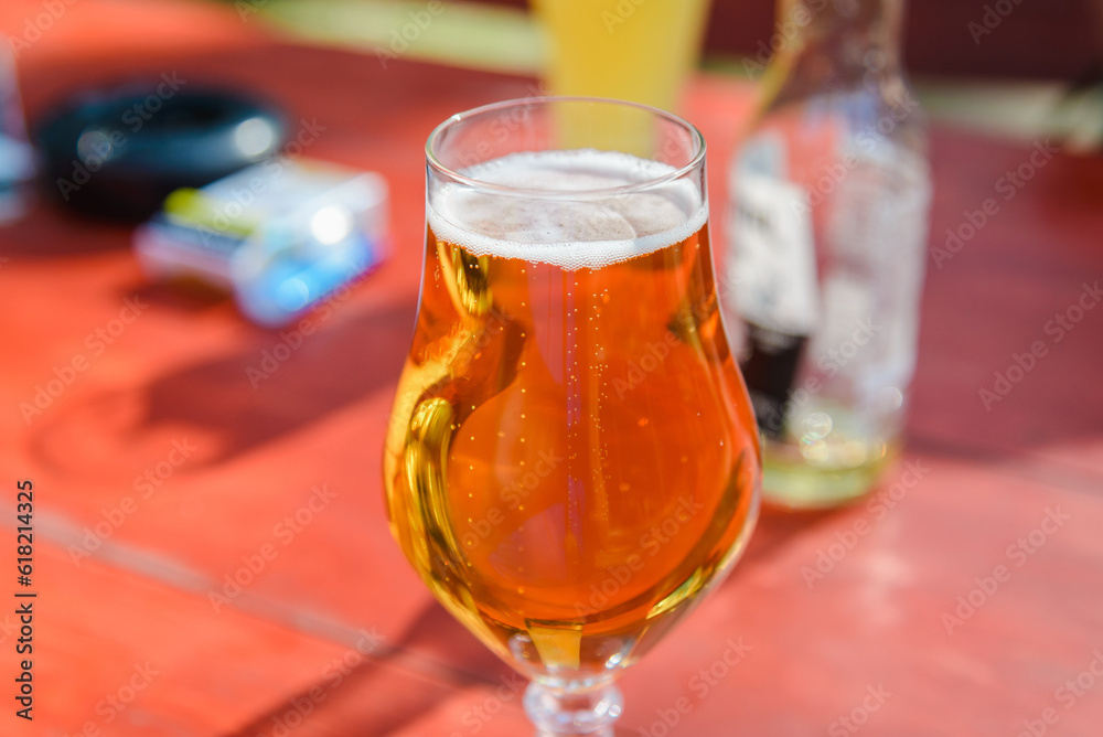 Glass of light beer on the wooden table.Glass of beer in nature.Empty bottle,a packet of cigarettes in a blurred background,summer day. Glass of light beer on the wooden table.Glass of beer in nature.Empty bottle,a packet of cigarettes in a blurred background,summer day.