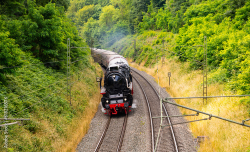 Historic steam train summer panorama on the main line between Hagen and Hamm, Germany. Big renovated express locomotive with old coaches in rural scenery on curved railway tracks near Dortmund.