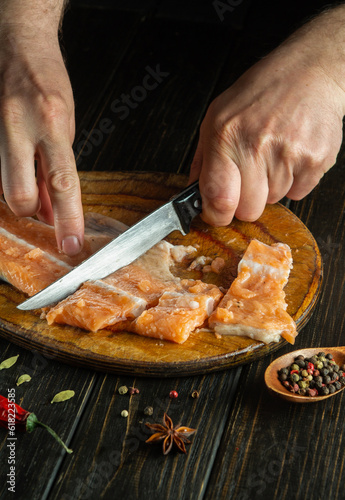 Chef cuts fresh raw fish with a knife on a wooden cutting board. Homemade delicious fish dish according to an old recipe. Trout cutting in the kitchen