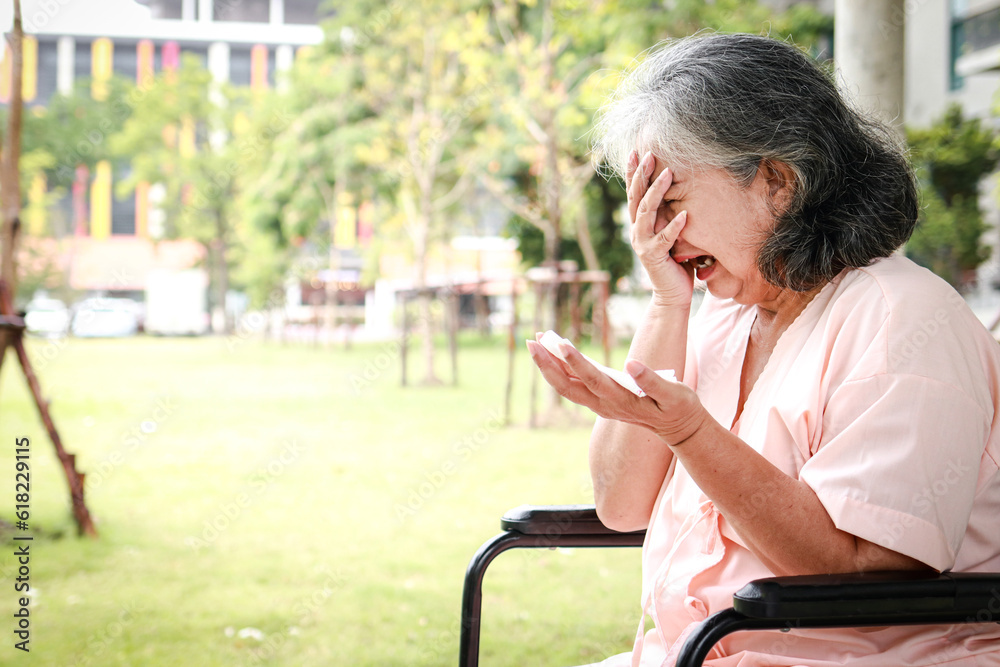 Fototapeta premium An elderly Asian female patient sits in a wheelchair in a hospital, she regrets her illness. Elderly disease concept, health insurance. copy space