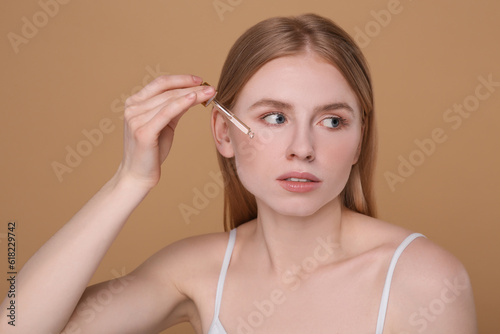 Woman applying essential oil onto face on light brown background