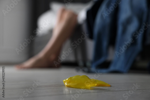Woman sitting on bed and unrolled condom indoors, closeup. Safe sex