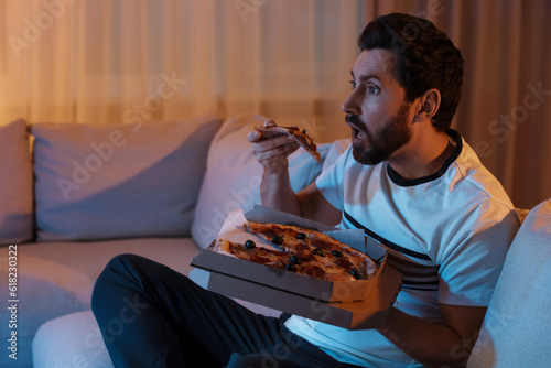 Man eating pizza while watching TV on sofa at night. Bad habit photo