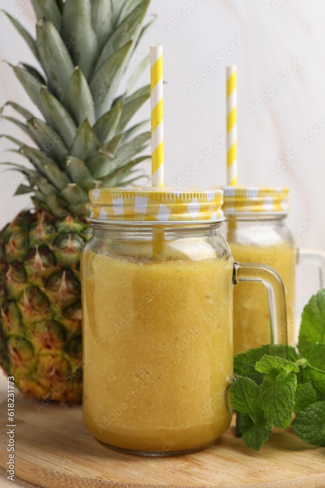 Tasty pineapple smoothie in mason jars, mint and fruit on wooden board, closeup Tasty pineapple smoothie in mason jars, mint and fruit on wooden board, closeup