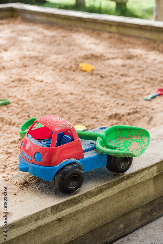 Red and blue toy truck carrying green shovel against sand pit in background, leisure and lifestyle concept illustration. Red and blue toy truck carrying green shovel against sand pit in background, leisure and lifestyle concept illustration.