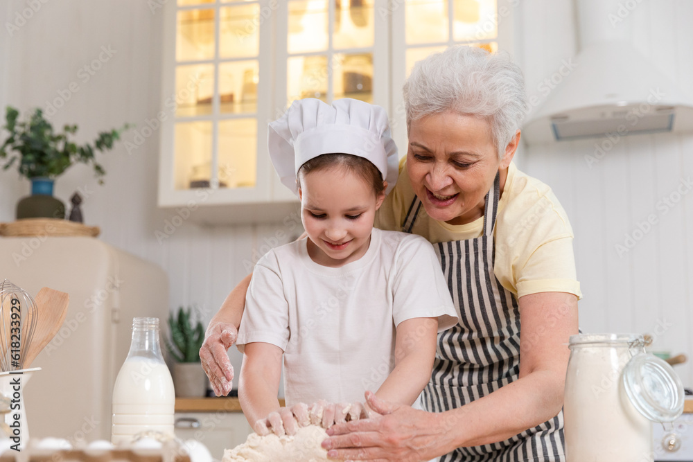 Happy family in kitchen. Grandmother and granddaughter child cook in kitchen together. Grandma teaching kid girl knead dough bake cookies. Household teamwork helping family generations concept Happy family in kitchen. Grandmother and granddaughter child cook in kitchen together. Grandma teaching kid girl knead dough bake cookies. Household teamwork helping family generations concept