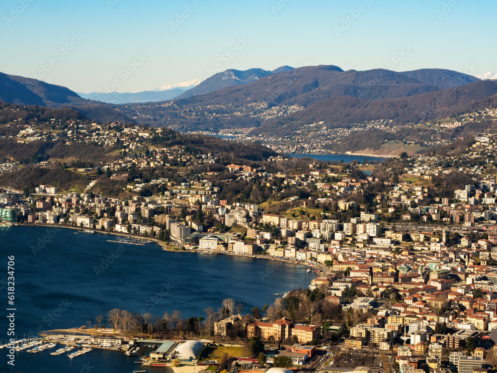 Aerial panorama in the morning of Lake Lugano, with the lake intensely blue in color; on its shore the city of Lugano; in the background the Swiss Alps