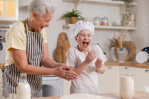 Happy family in kitchen. Grandmother and granddaughter child cook in kitchen together. Grandma teaching kid girl knead dough bake cookies. Household teamwork helping family generations concept