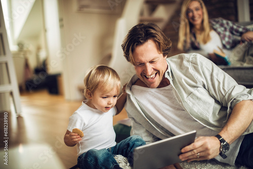 Father and son using a digital tablet at home while the mother is behind them on the couch