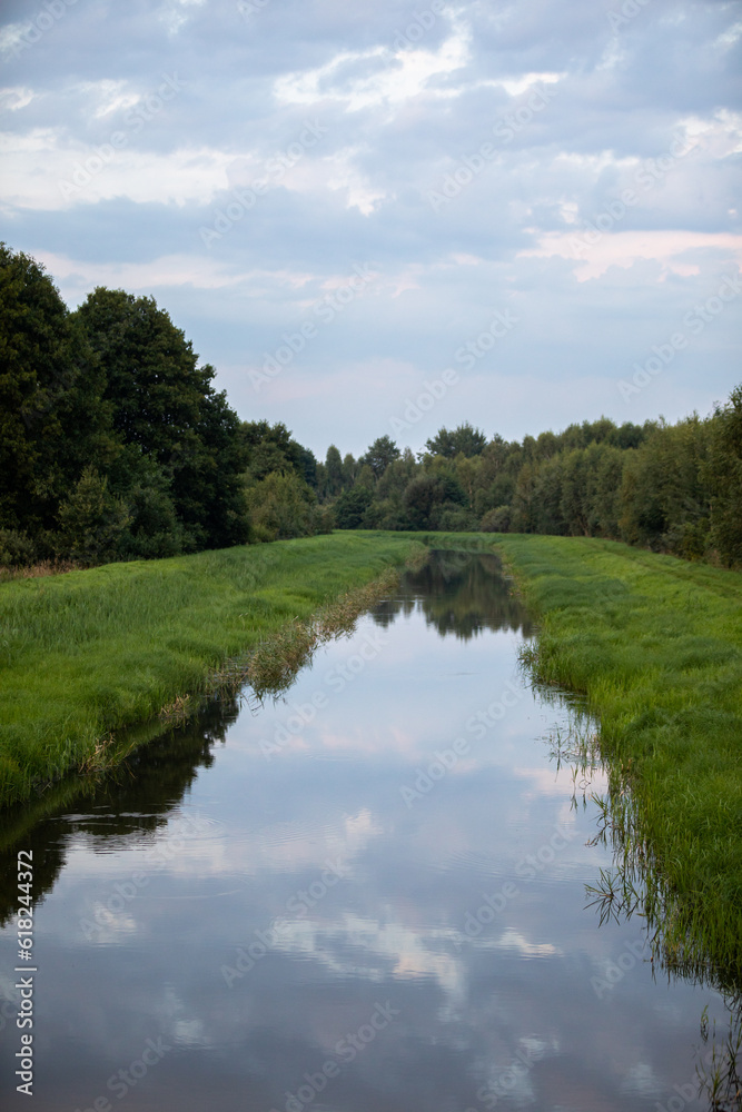 A slow-flowing wide river among lush green grasses and tall trees.