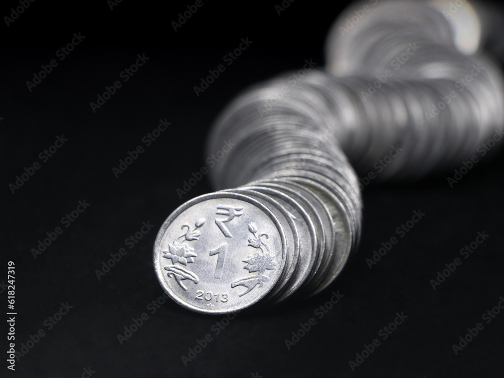1 (one) rupee coins of india made of silver stacked together in a curved row shaped like a snake in closeup isolated in a black background 1 (one) rupee coins of india made of silver stacked together in a curved row shaped like a snake in closeup isolated in a black background