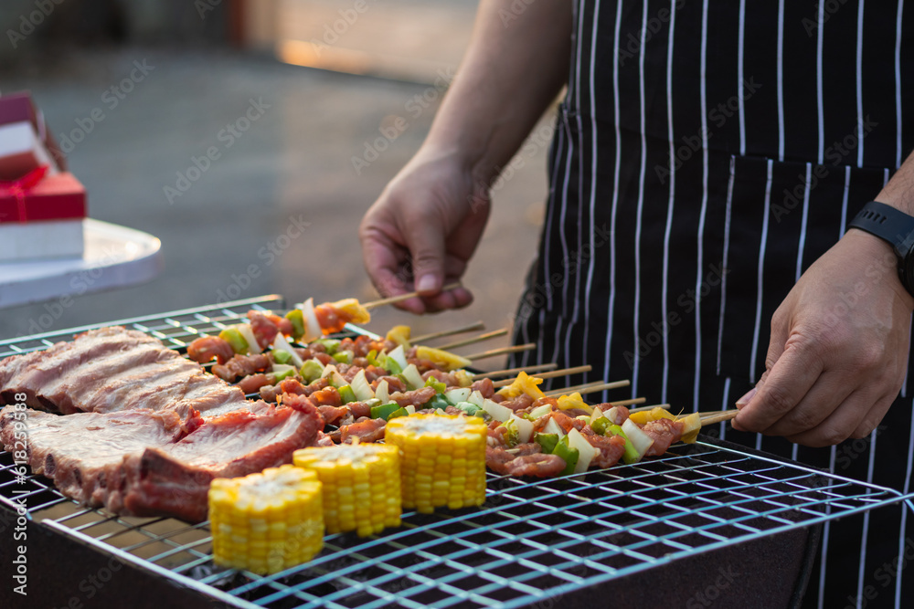 Meat and skewers ingredients for barbecue party are placed on grill to cook barbecue and make it ready for family to join barbecue party tonight.  party background image has Copy Space for text.