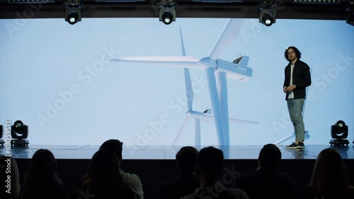 Caucasian man speaker presenting on the stage during ecological renewable energy conference. Future technology meetup. Talks about green energy sources, wind turbines, solar power photo