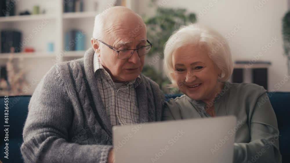 Smiling couple in their 60s choosing new house on laptop, online shopping, app Smiling couple in their 60s choosing new house on laptop, online shopping, app