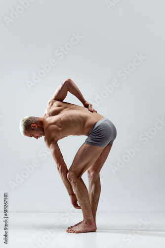 Handsome, young man with fit, relief, strong, muscular body posing shirtless in underwear on grey studio background. Concept of male natural beauty, body care, health, sport, fashion, ad, statue art photo