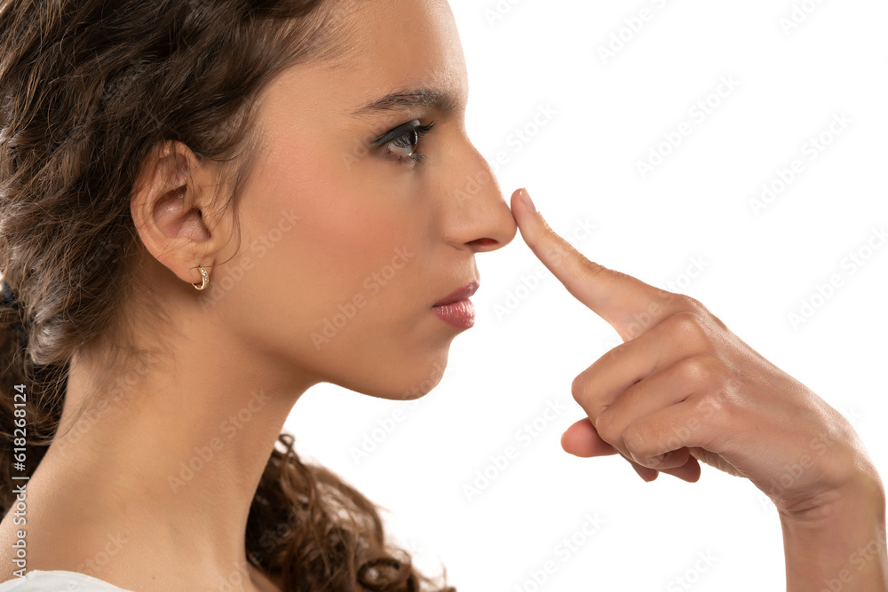 Profile portrait of a beautiful young woman touches her nose with a hump on white background Profile portrait of a beautiful young woman touches her nose with a hump on white background