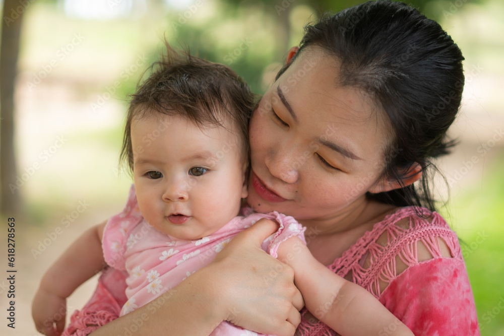 Asian mum and little child - young happy and beautiful Korean woman playing on city park with adorable and cheerful baby girl in mother and daughter love and bonding